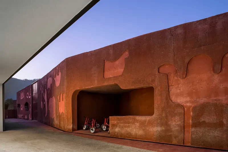 Rammed earth wall with sculpted relief cutouts and wheelchairs stored in a recessed niche