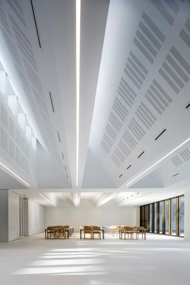 White ceiling with radial perforated panels and central skylight illuminating the white resin floor below