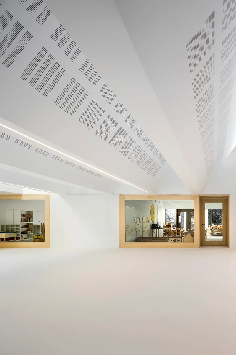 Angled view of the ceiling showing diagonal perforated panels and timber-framed windows to interior spaces