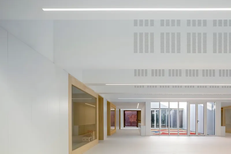 Corridor with timber door frames, perforated ceiling panels, and glazed courtyard opening at the end