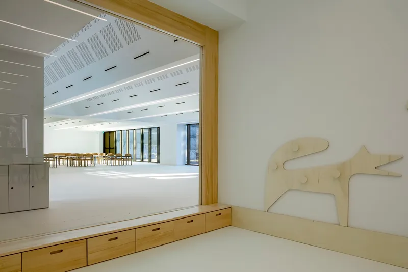 Built-in timber bench with storage drawers framing a view into a daylit multipurpose room