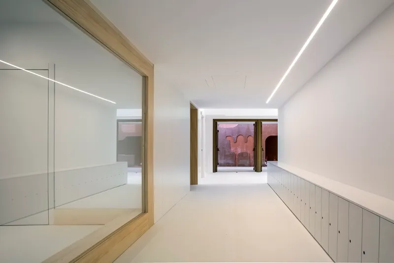 White corridor with timber door frames and rows of metal lockers leading toward windows