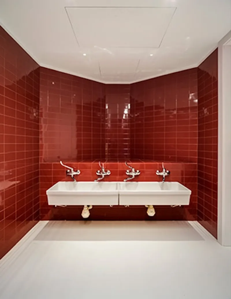 Restroom with glossy red tile walls and twin wall-mounted sinks with chrome faucets
