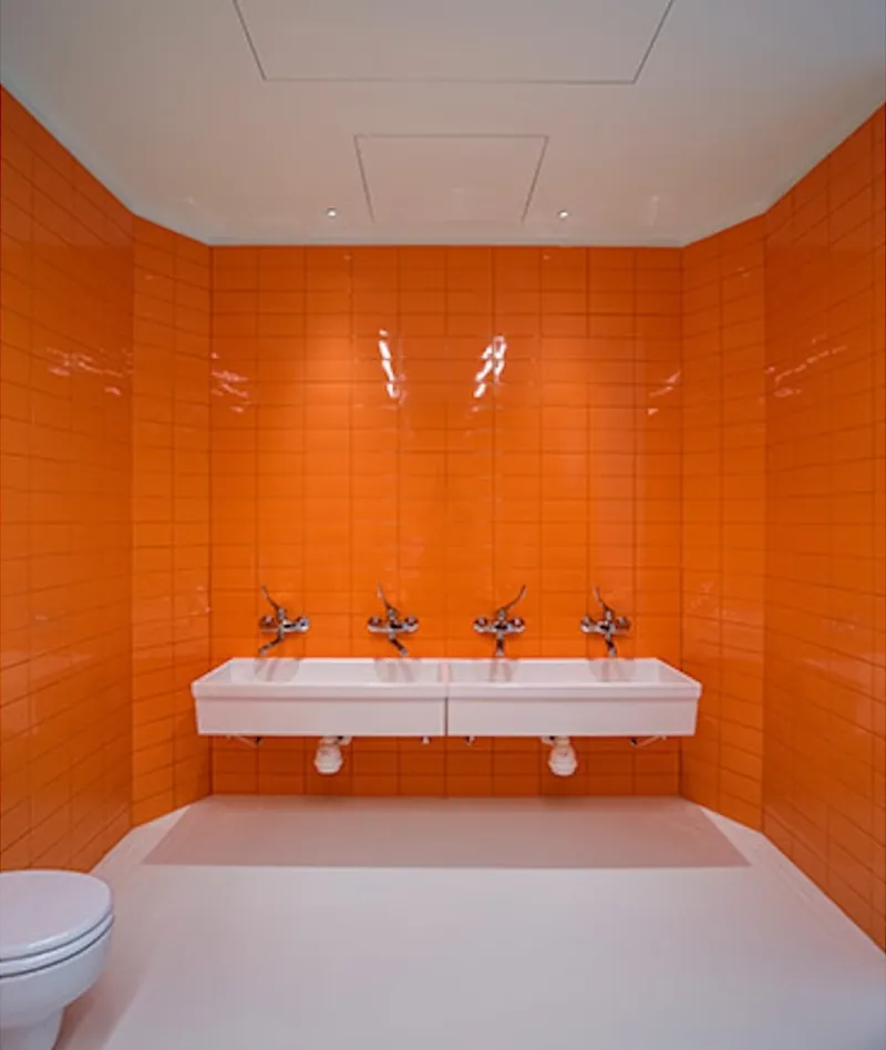 Restroom with glossy orange tile walls and twin wall-mounted sinks with chrome faucets