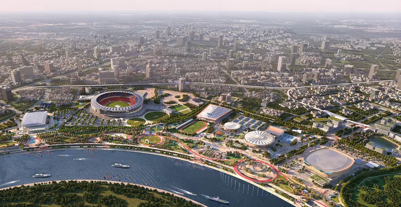 Aerial view of a sports complex and waterfront development with a stadium and landscaped pavilions beside a river