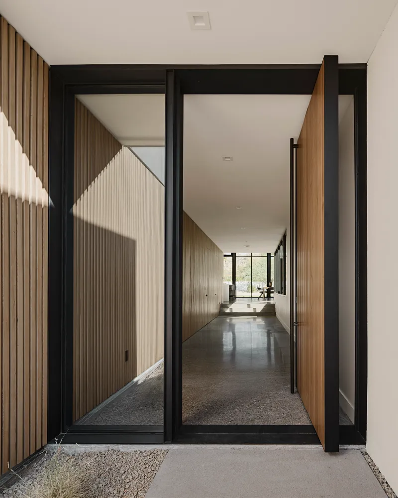 Pivoting timber door in black steel frame opening to polished concrete hallway