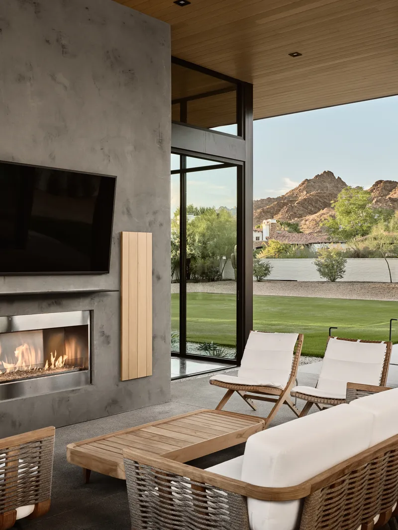 Living room with concrete fireplace wall and floor-to-ceiling glazing framing view of lawn and rocky hillside beyond