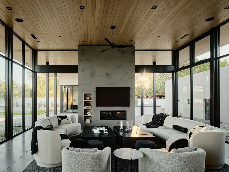 Open living space with central concrete fireplace volume flanked by full-height glazing and continuous wood ceiling plane