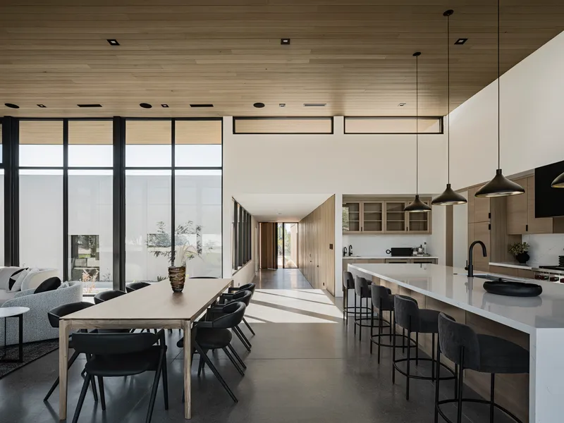 Combined dining and kitchen area with long white island under horizontal wood ceiling and clerestory windows above