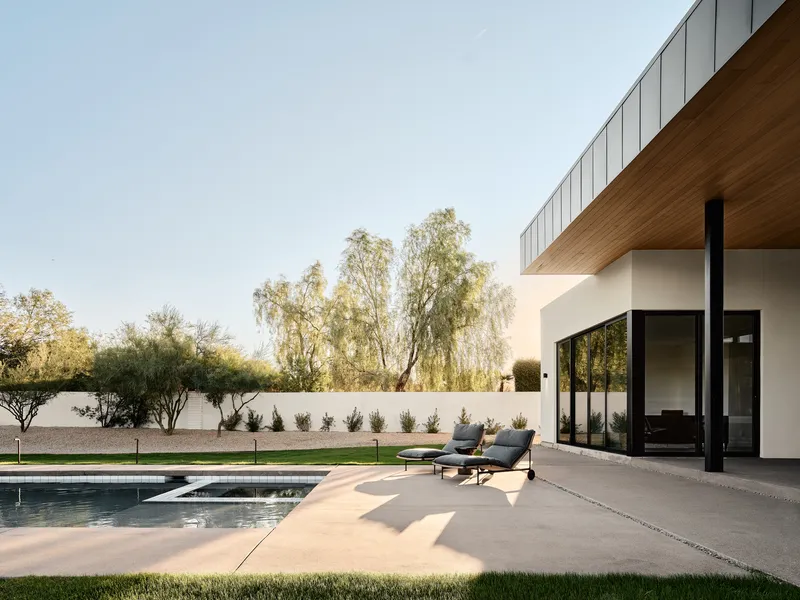 Pool terrace with concrete deck and timber soffit overhang beneath willow trees in afternoon light