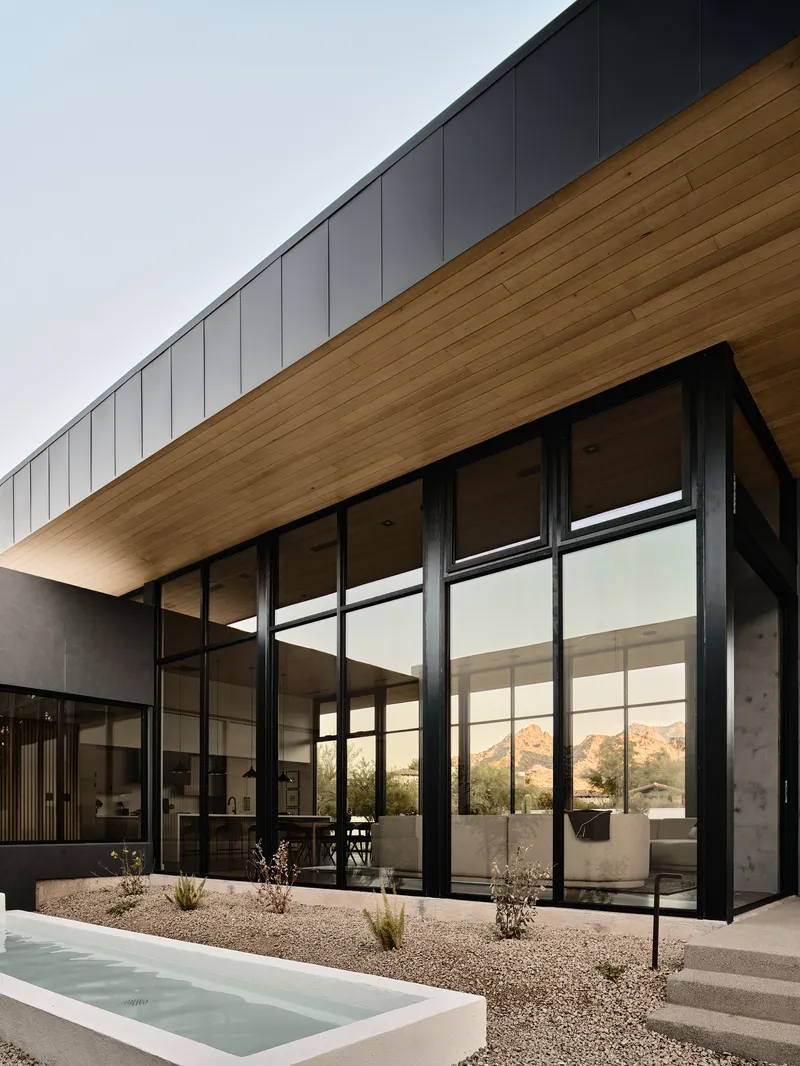 Corner glazing beneath cantilevered timber soffit and metal panel roof at sunset