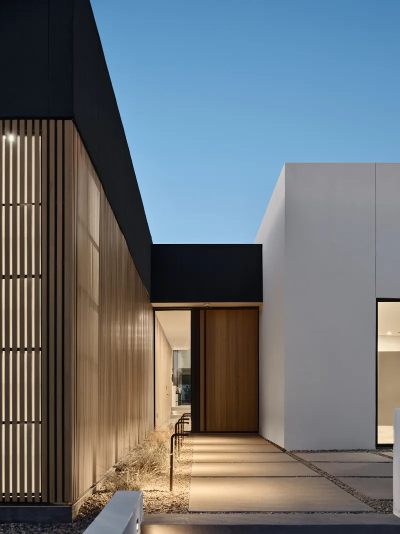 Entry courtyard with timber slat screen wall and paved walkway under clear sky
