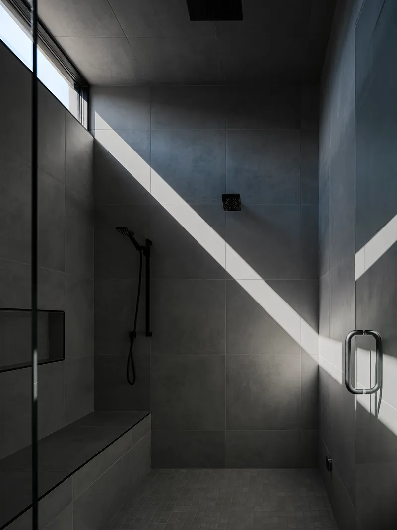 Tile-clad shower room with high clerestory window casting sharp shadows across the walls