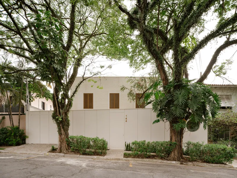 Street view of the white rendered facade with timber shuttered windows framed by overhanging trees
