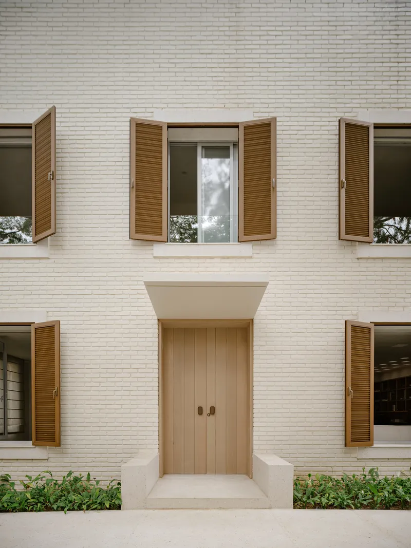 Symmetrical facade with white brick, recessed timber door and wooden louvered shutters flanking upper and lower windows