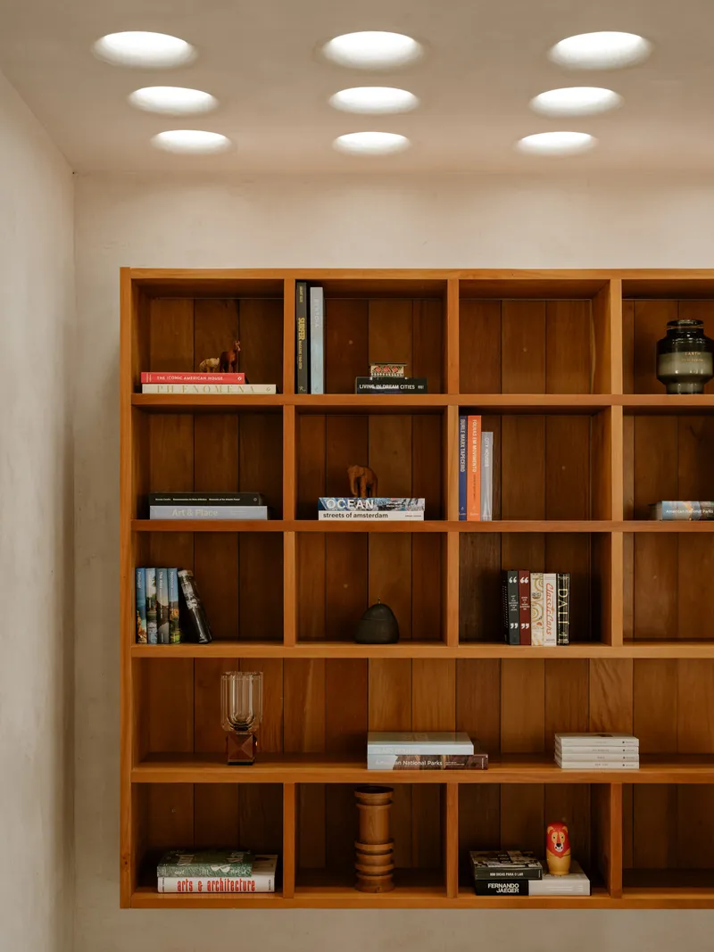 Built-in timber shelving grid with books and objects beneath a ceiling perforated with circular light wells