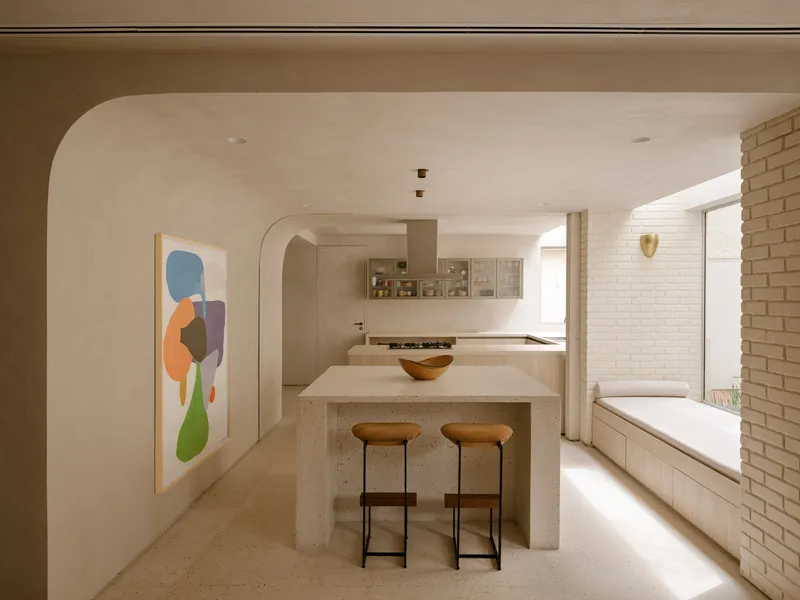 Kitchen with terrazzo island and two stools beneath arched openings and white brick bench seating