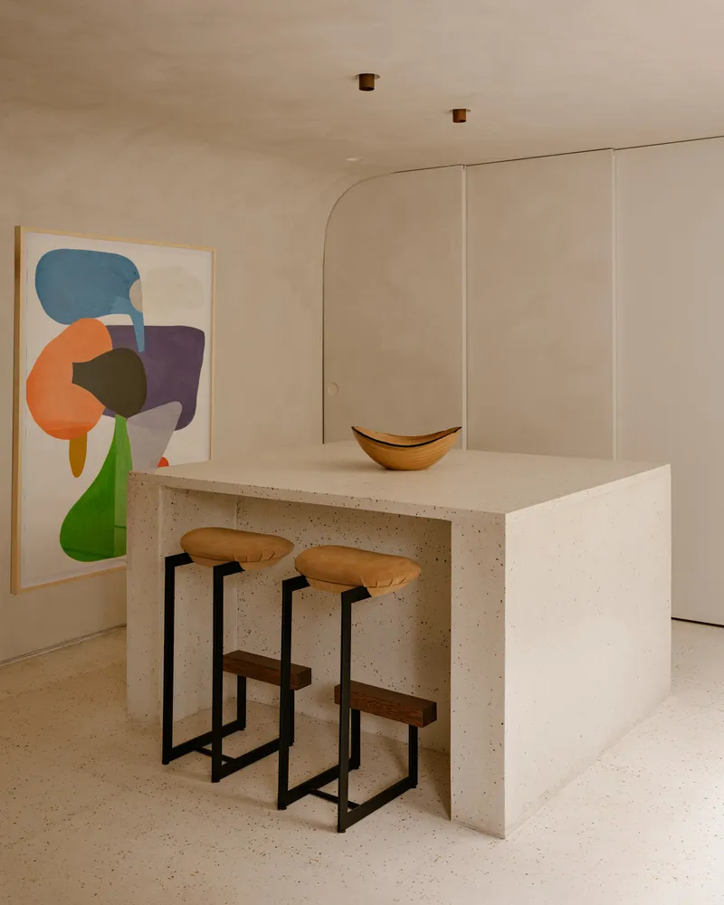 Kitchen island in terrazzo with bar stools facing paneled cabinetry and abstract artwork on the wall