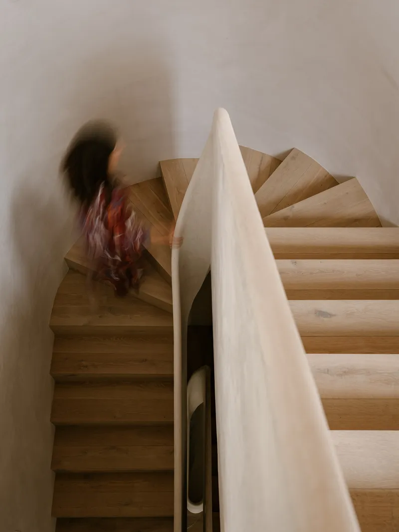 Timber spiral staircase with white plastered walls and a figure ascending in motion blur