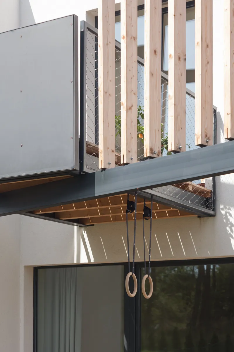 Steel frame and vertical wooden slats form a secondary skin, enhancing shading, depth, and spatial buffering.