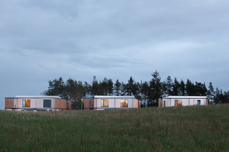 Minimal cubic forms sit lightly within the landscape, opening selectively toward distant views while maintaining enclosure.