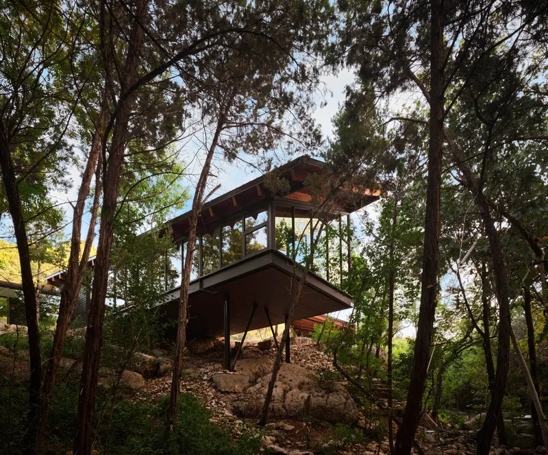 Two-story structure on a rocky hillside nestled among tall eucalyptus trees at dusk