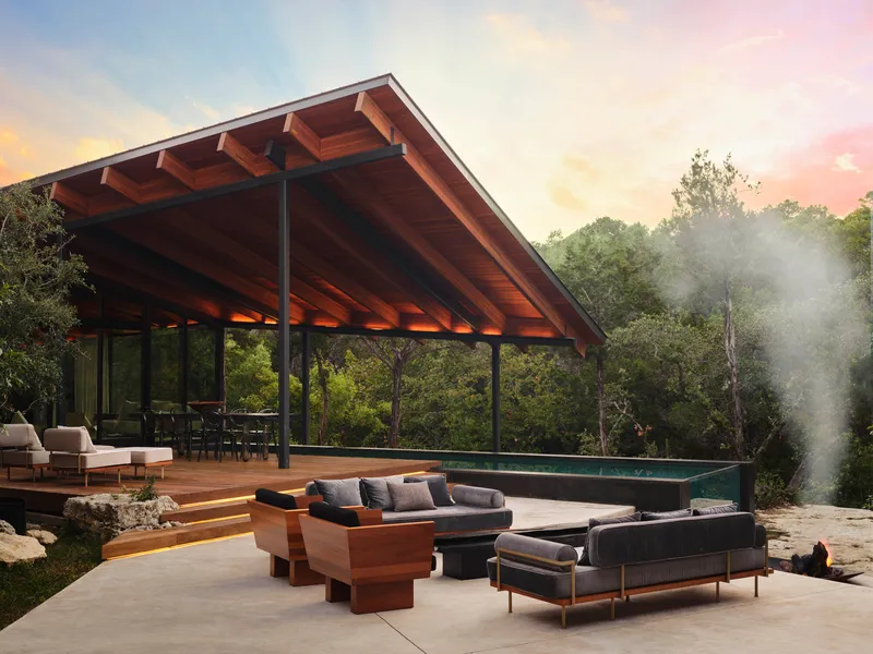 Open pavilion with exposed timber beams and steel columns overlooking a terrace with pool at sunset