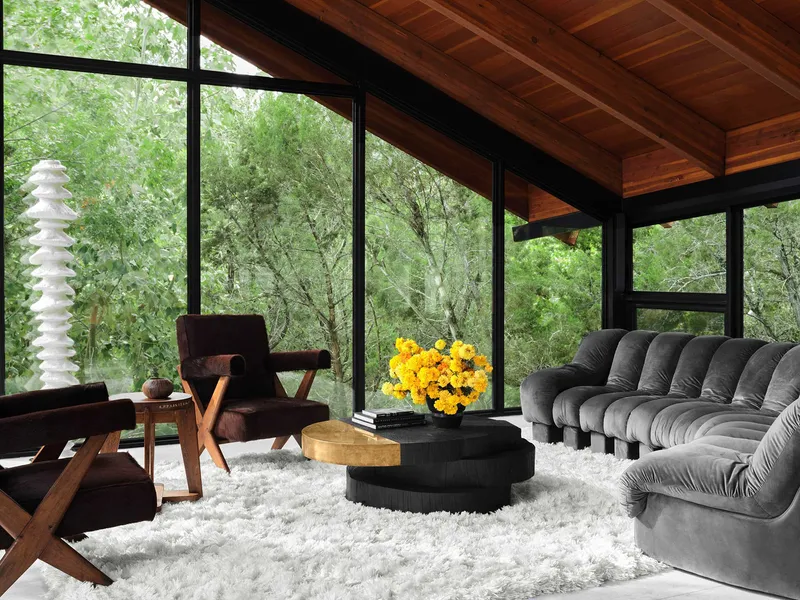 Living area with black-framed windows, wood ceiling, and views into surrounding forest canopy