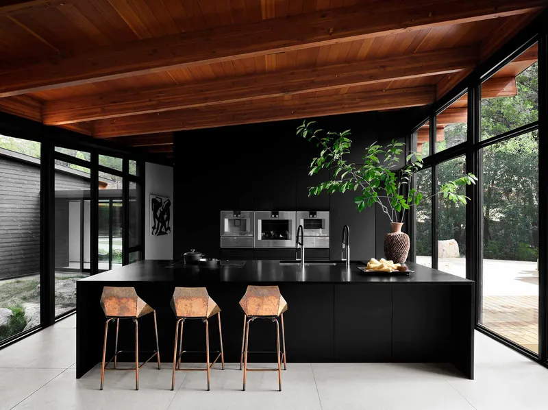 Black kitchen island with integrated sink beneath wood plank ceiling and full-height glazing