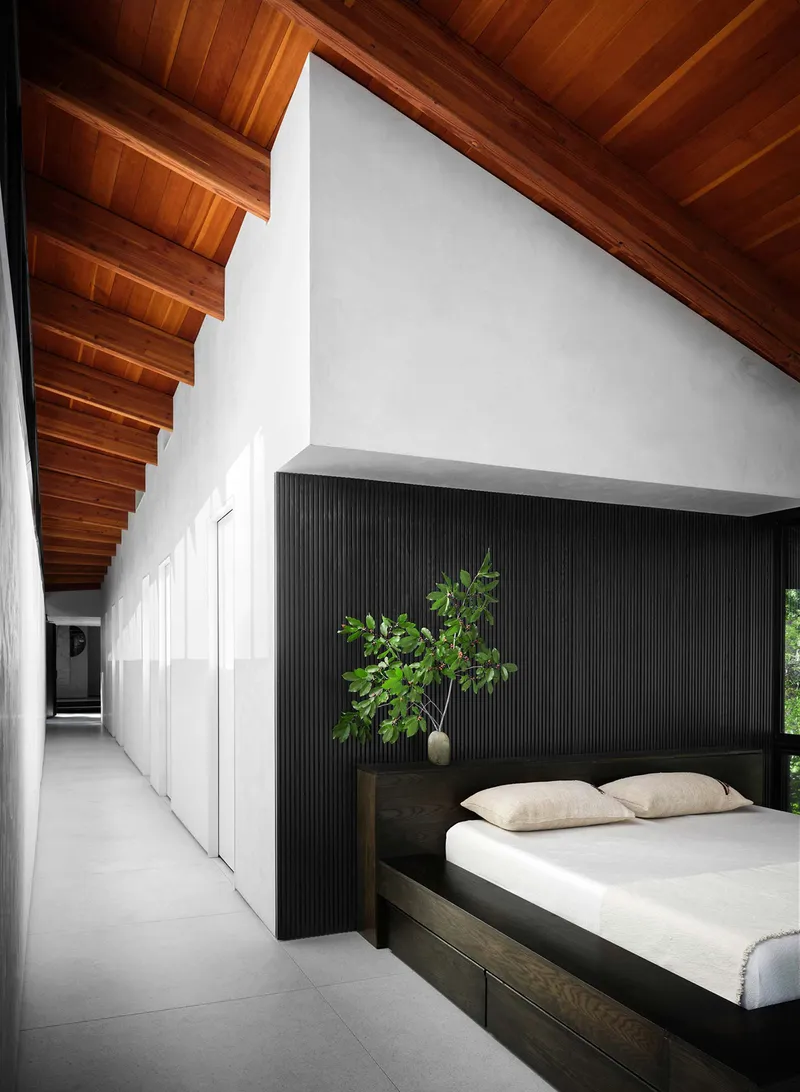 Bedroom with ribbed black headboard wall below sloped wood ceiling and polished concrete floor