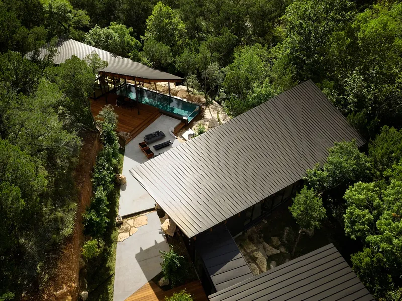 Aerial view of corrugated metal roofs and outdoor terraces nestled among green tree canopy