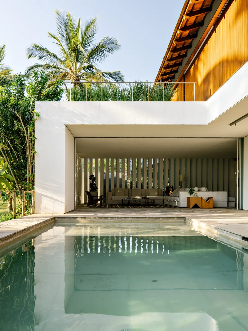 Swimming pool terrace with white stucco volume and vertical timber slat screen in dappled sunlight