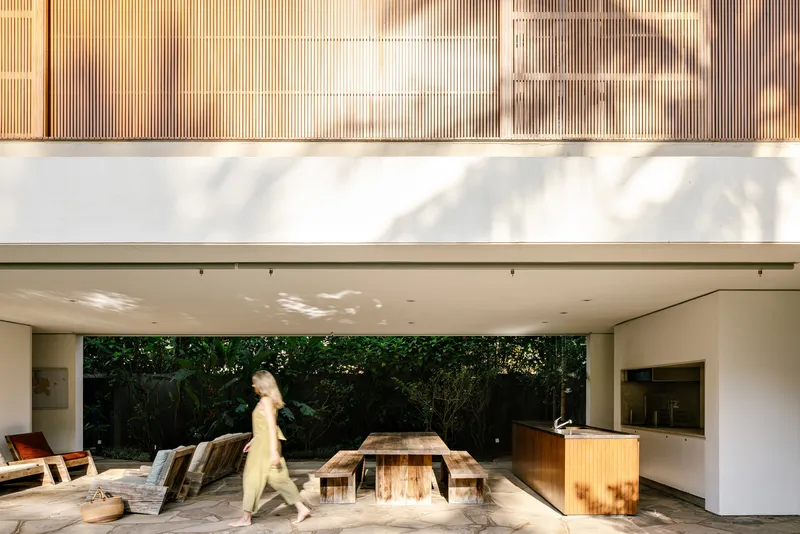 Covered terrace with timber dining table and figure walking past vertical timber cladding above