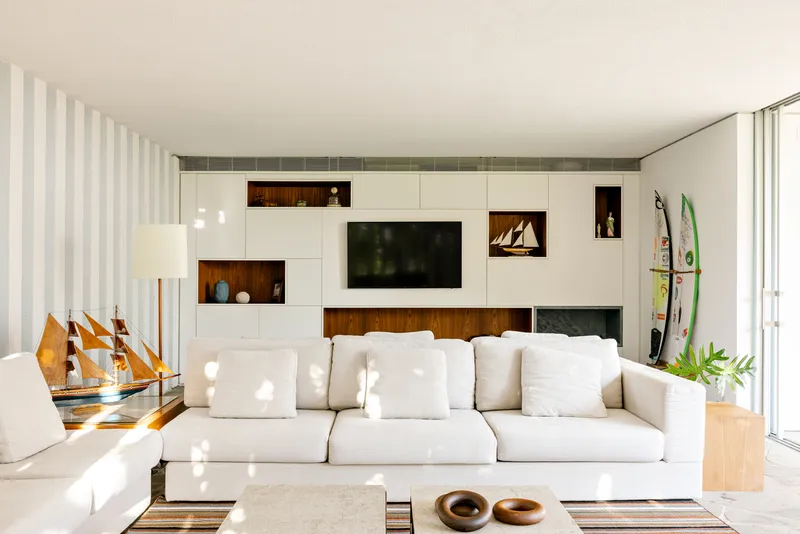 Living room with white storage wall featuring timber insets and vertical sheer curtains