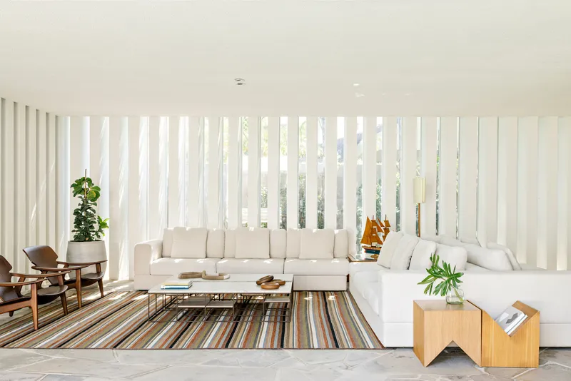 Living room with vertical white louvres filtering daylight onto grey marble flooring and a striped rug
