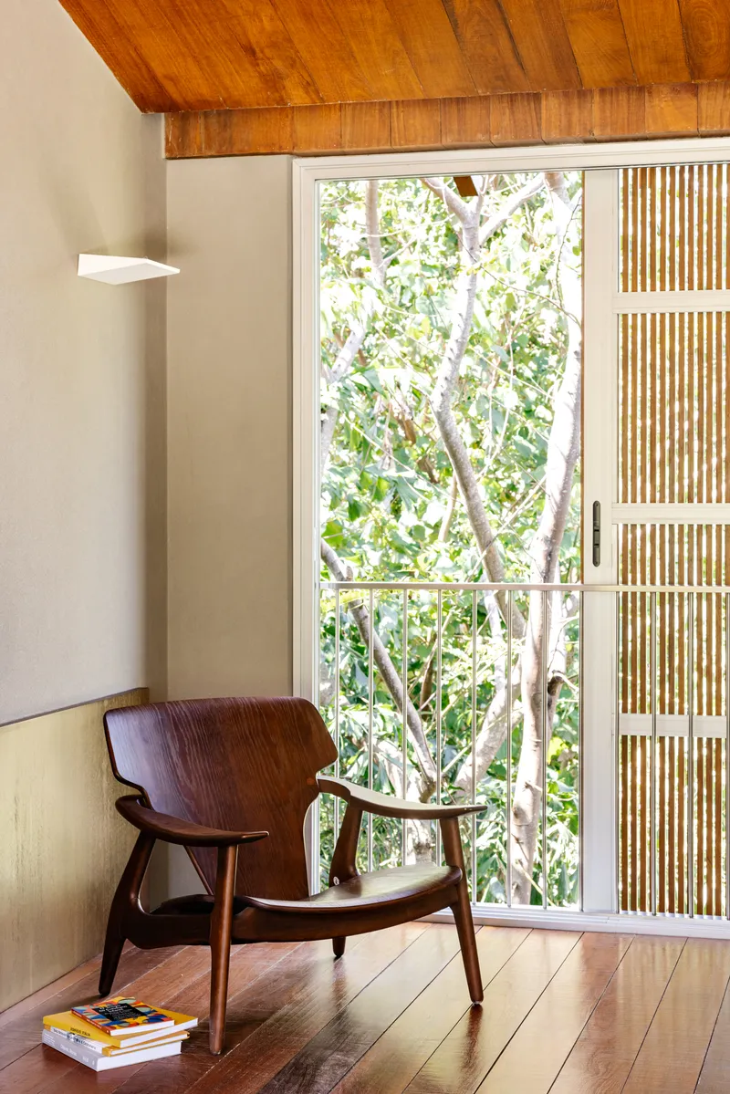 Interior corner with timber-panelled ceiling and glazed door opening to a garden with white-barked trees