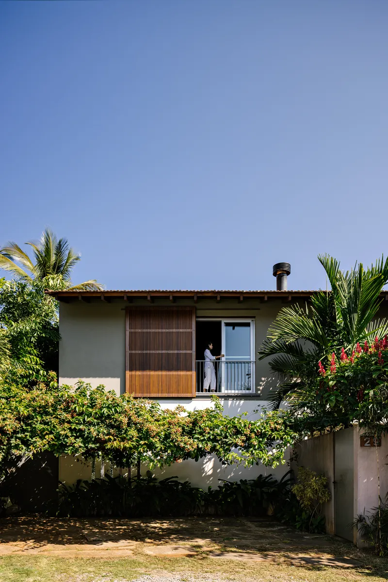 Upper balcony with sliding timber screen and figure standing at metal railing behind planted shrubs
