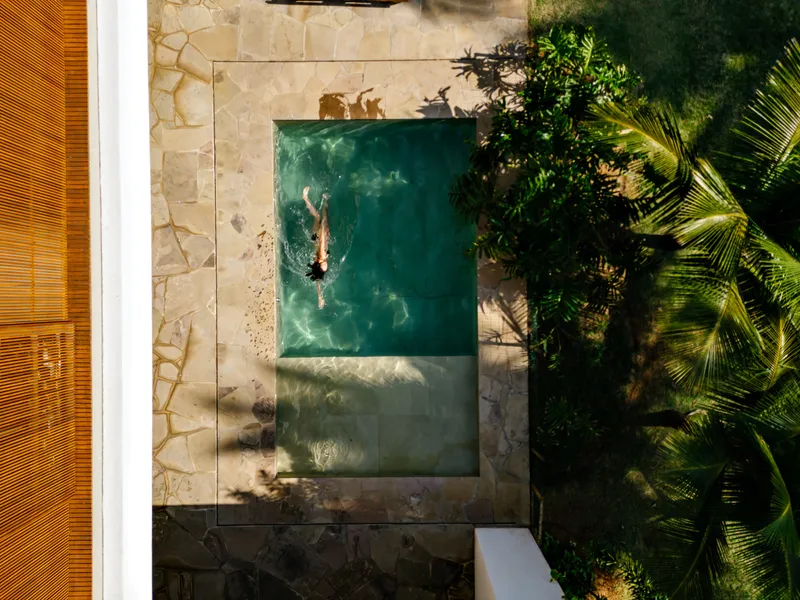Aerial view of swimmer in rectangular pool surrounded by sandstone paving and palm trees