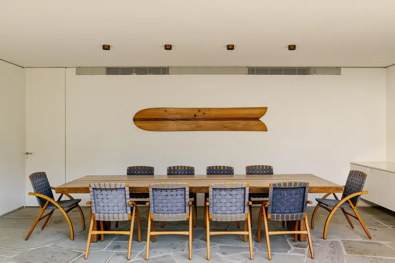 Dining area with timber table, woven chairs, and wooden canoe mounted on white wall