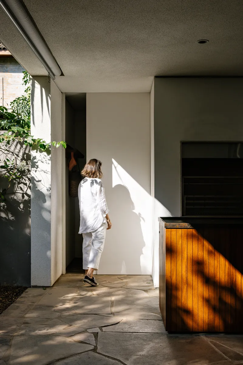 Entry passage with woman walking through sunlit corridor beside timber-clad counter and planted courtyard