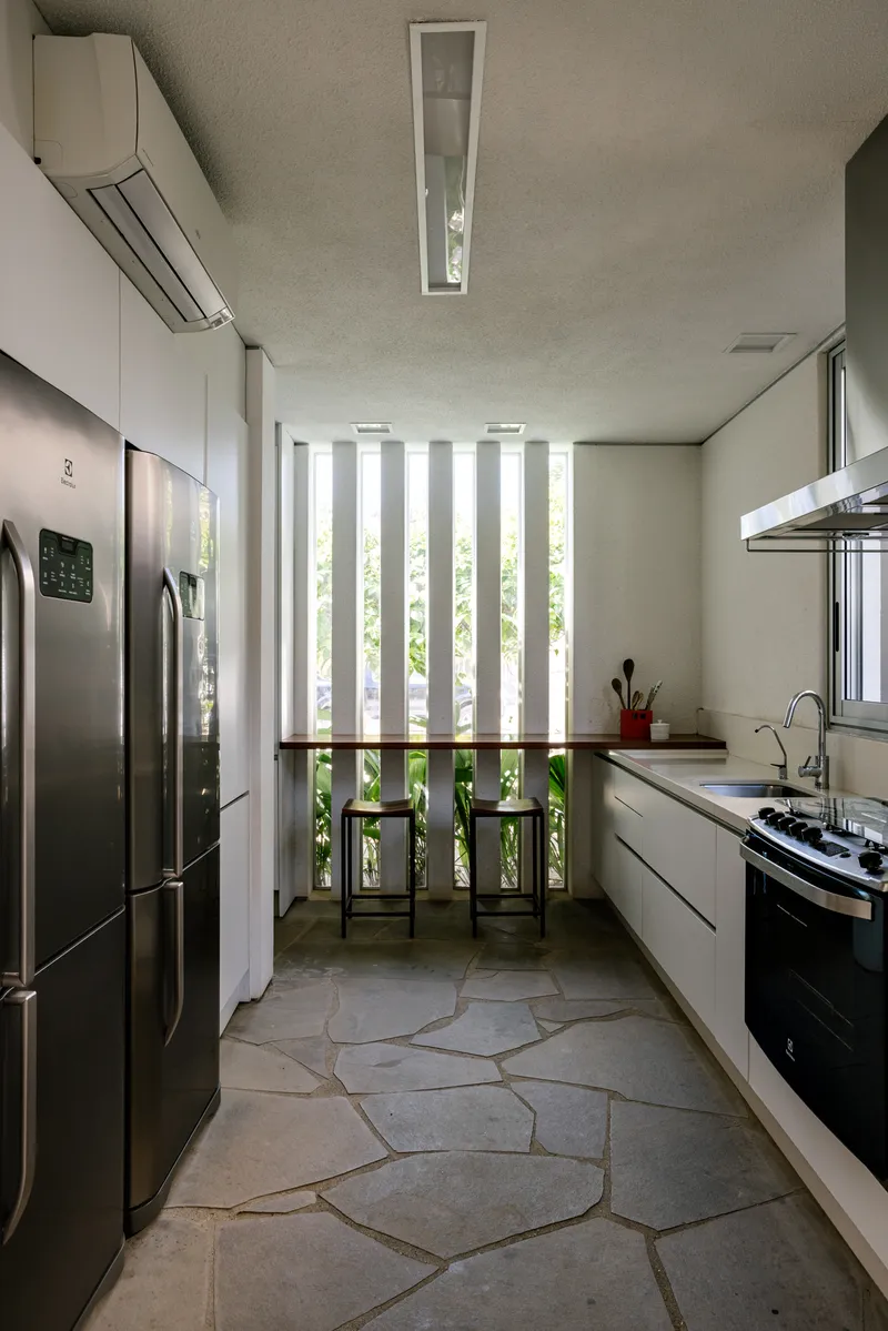 Galley kitchen with irregular stone floor, vertical slatted screen, and view to garden vegetation