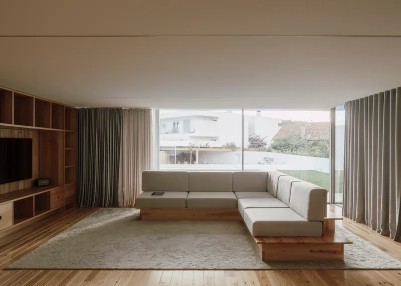 Living room with corner sofa facing full-height glazing overlooking lawn and neighboring rooftops