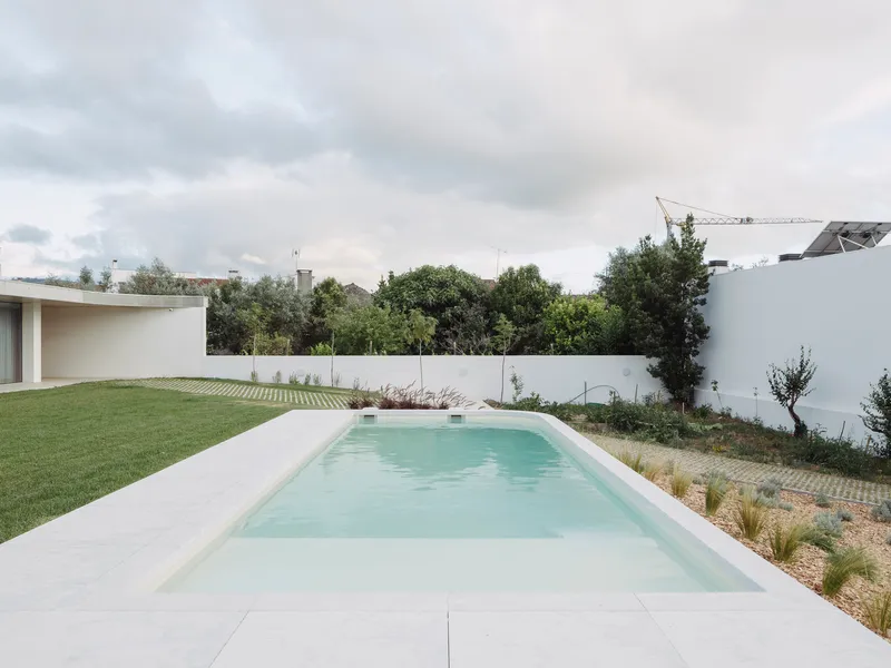 Rectangular pool with pale water flanked by white paving, lawn, and planted beds enclosed by white walls