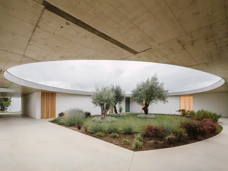 Central courtyard with circular roof opening above olive trees and planted beds with grasses