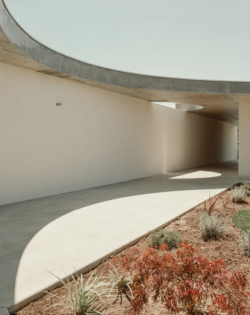 Curving passage beneath board-formed concrete soffit with circular roof openings casting light pools