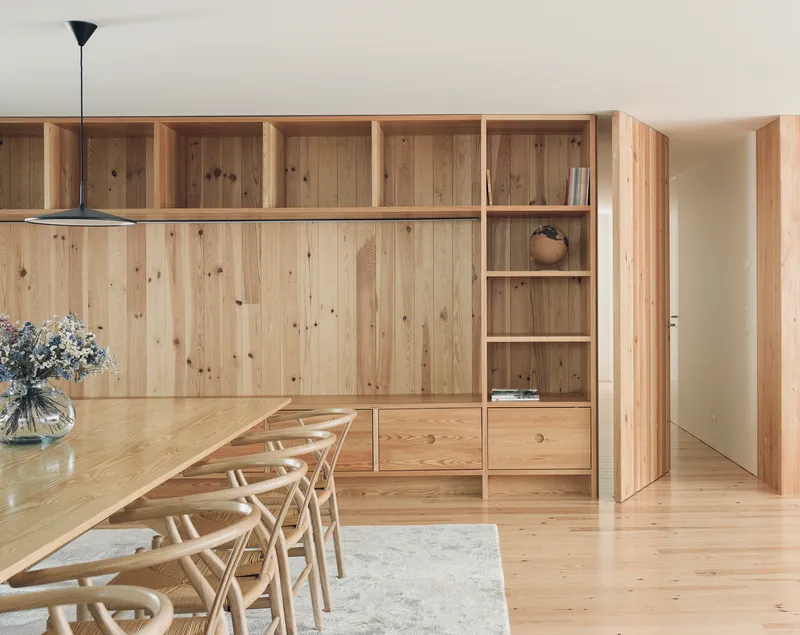 Dining area with timber storage wall, open shelving, and chairs around a long table
