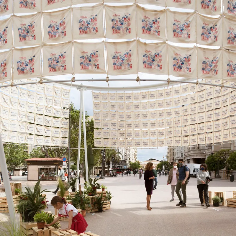Interior view under the textile canopy showing printed fabric panels and pedestrians among potted plants