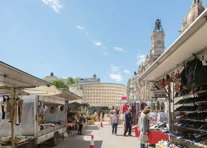Open-air market stalls with white canopies lining the plaza in front of a patterned stone facade