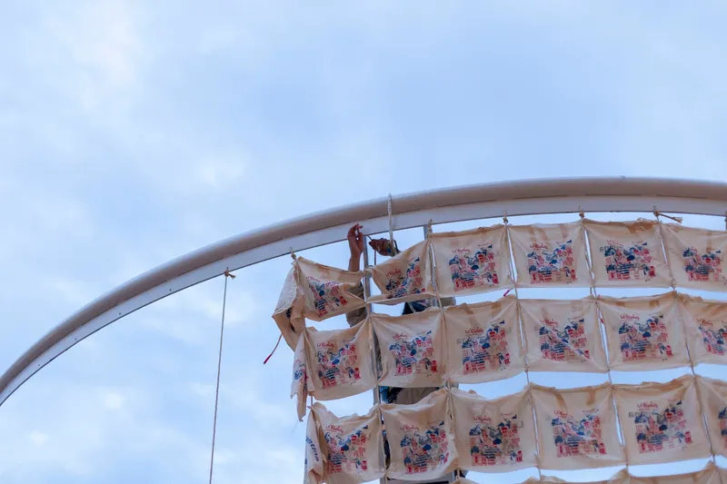 Close-up of curved steel armature with printed fabric banners suspended from cables against overcast sky