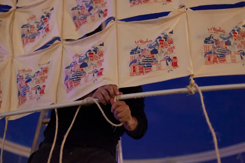 Hands tying rope knot on frame below printed textile panels at dusk